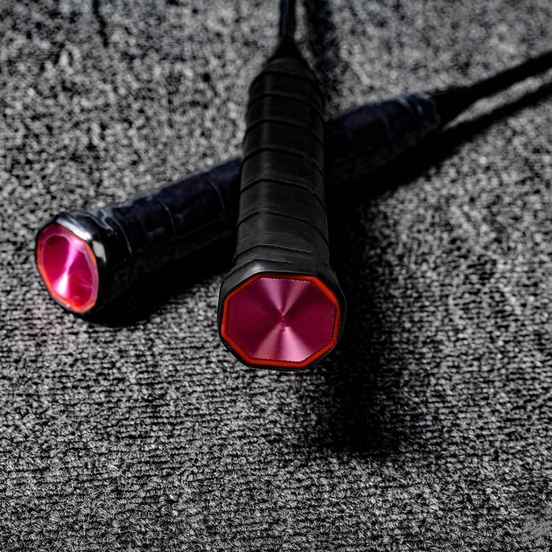 Close-up of the handles of two carbon fiber badminton rackets, featuring black grips and pink octagonal end caps with a textured finish