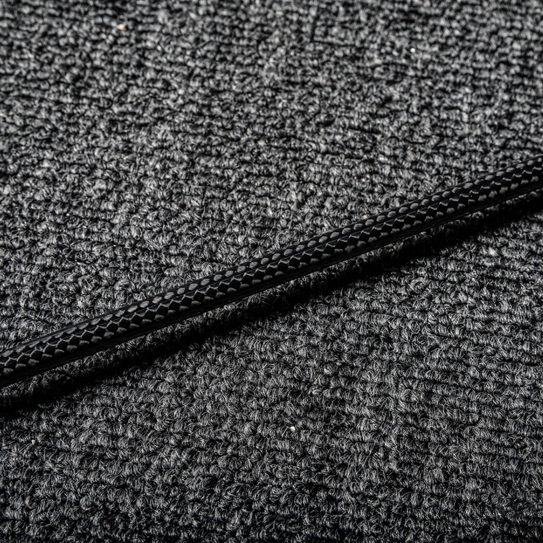 Close-up of a carbon fiber badminton racket shaft showcasing its distinct textured pattern, laid on a gray textured surface.
