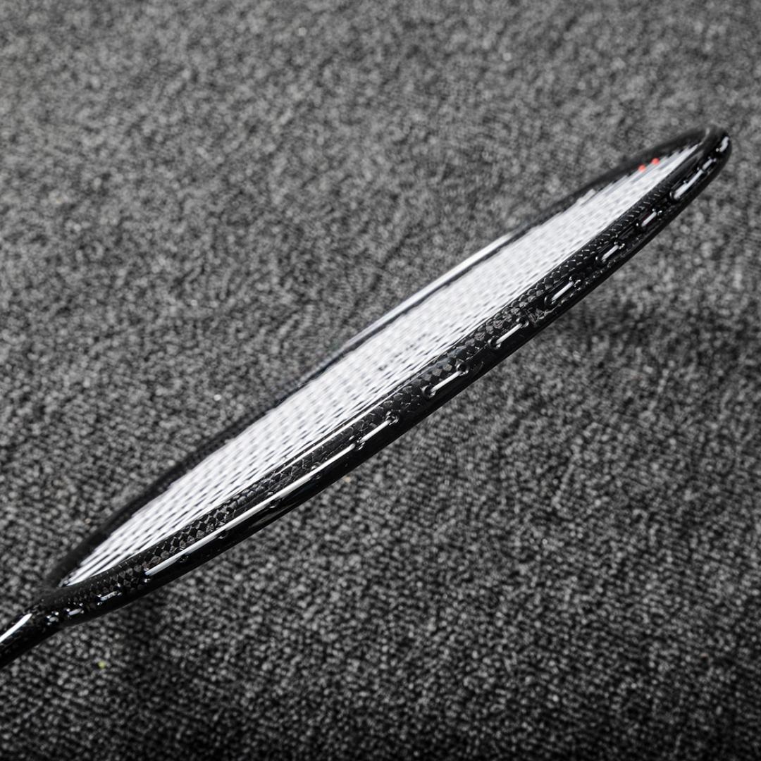 Close-up of a carbon fiber badminton racket frame showcasing its textured surface and white strings, positioned on a gray textured background.