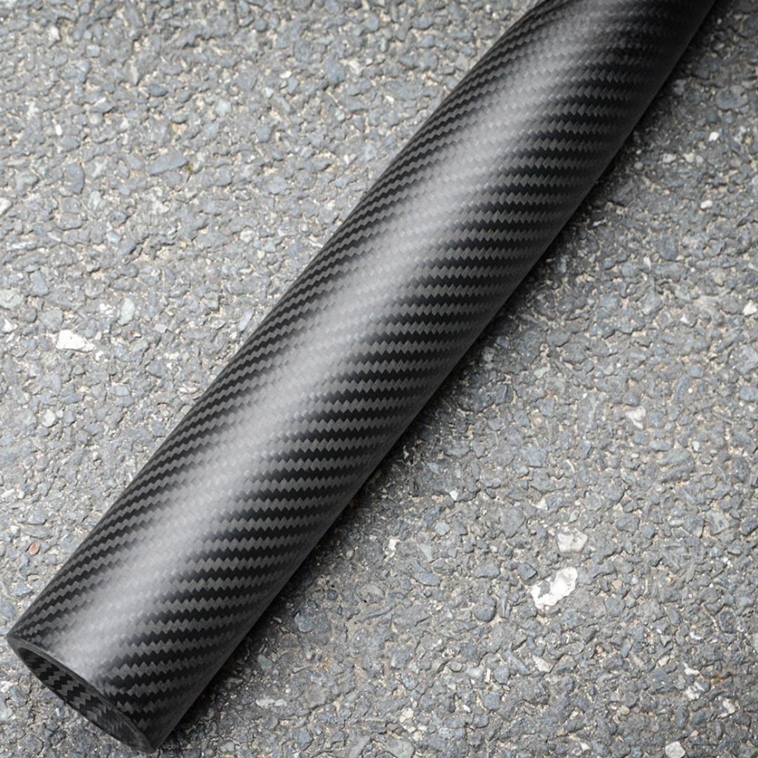 Close-up of a 3K carbon fiber baseball bat with a distinct weave pattern, placed on an asphalt surface.