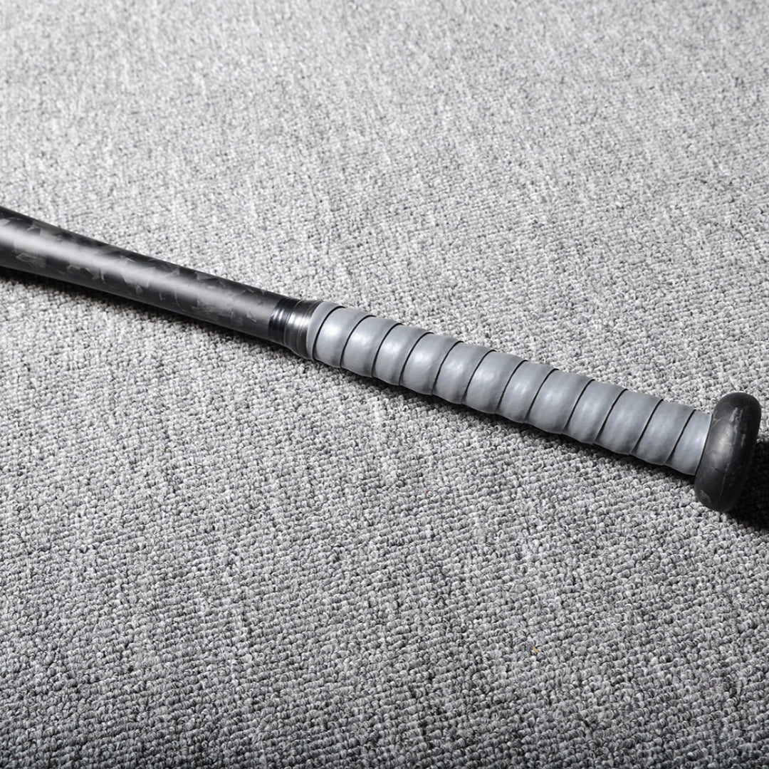 Close-up of the handle of a forged carbon fiber baseball bat, featuring a gray textured grip, laid on a gray textured surface.