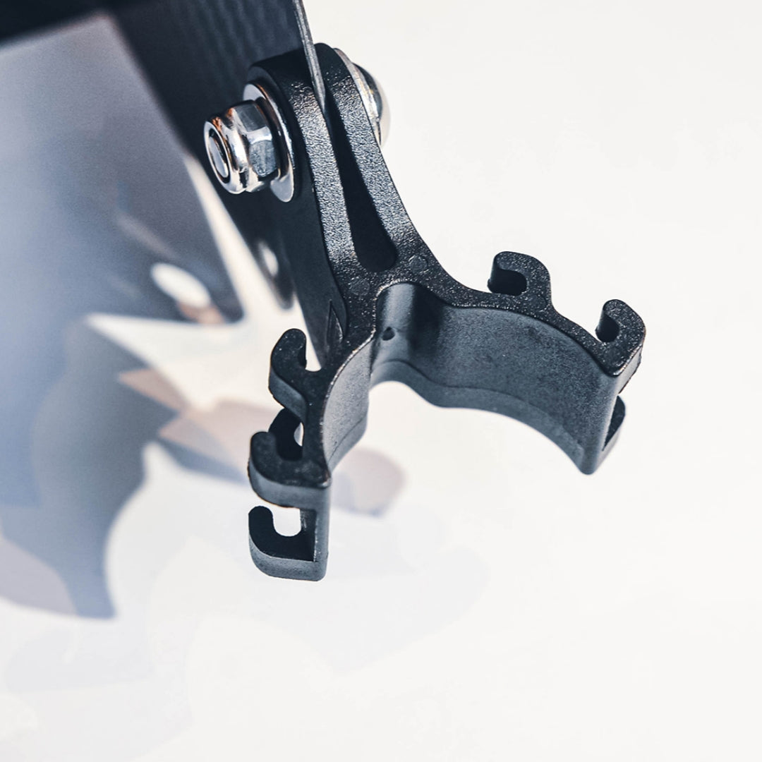 Close-up detailed view of the mounting bracket for a carbon fiber bicycle number plate, showcasing the black plastic/metal clamp and metal bolt assembly.