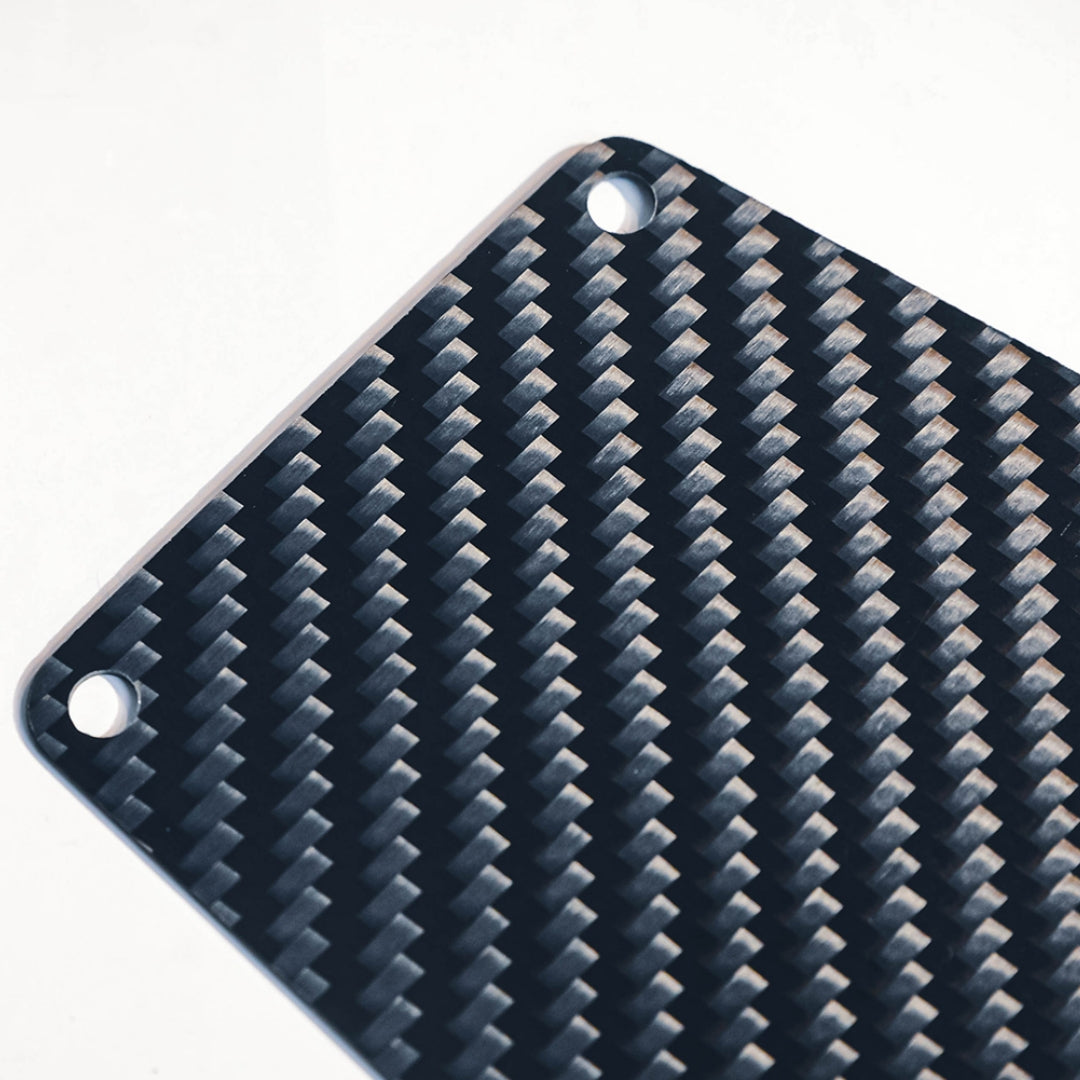 Close-up detail of a carbon fiber bicycle number plate, showcasing its distinctive woven pattern and mounting holes.