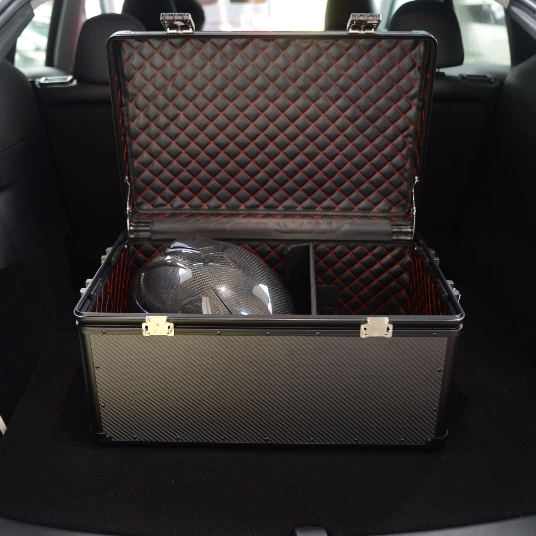 Close-up detail of an open large 3K carbon fiber car storage trunk with a quilted interior featuring red stitching, containing a carbon fiber helmet, placed in a car trunk.