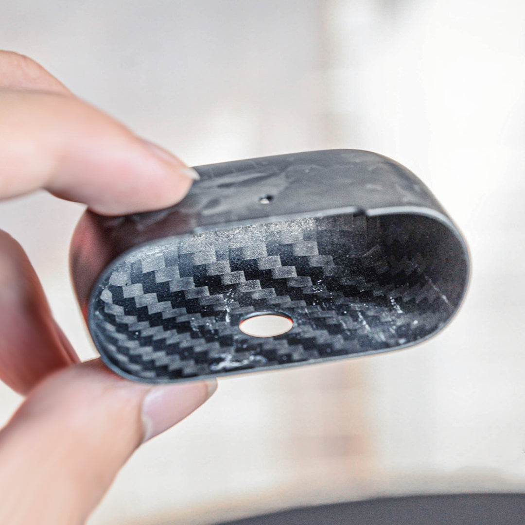 Close-up of the interior of the lower half of a forged carbon fiber AirPods case, held in a hand against a soft, blurred background, showcasing its unique marbled texture and structural details.