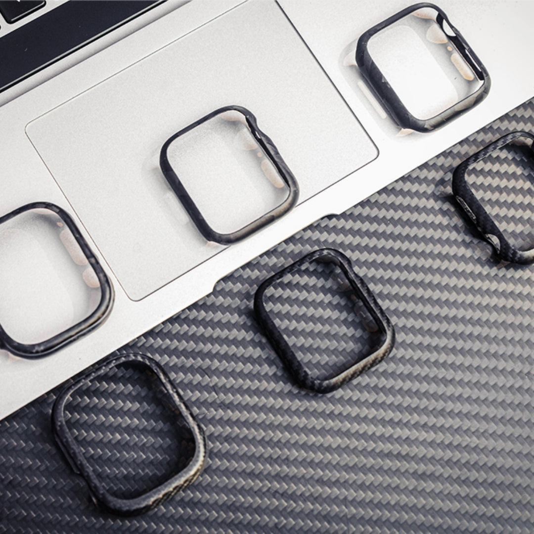 Close-up of six carbon fiber Apple Watch cases showcasing their detailed woven textures, arranged on a laptop and a carbon fiber-textured surface.