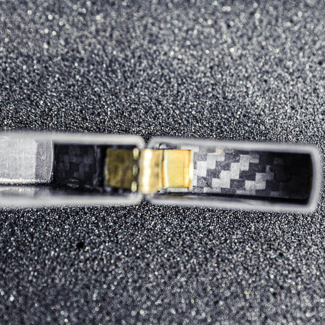 Close-up of the hinge area of a 3K carbon fiber Zippo lighter case, showcasing the detailed carbon fiber weave pattern inside, placed on a textured, glittery dark surface.