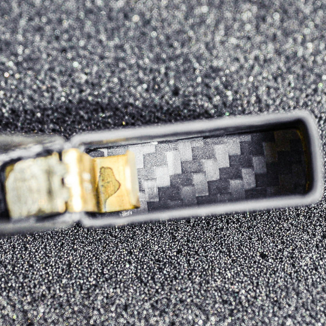 Close-up of the interior hinge area of a 3K carbon fiber Zippo lighter case, showcasing the detailed carbon fiber weave pattern, placed on a textured glittery dark surface.