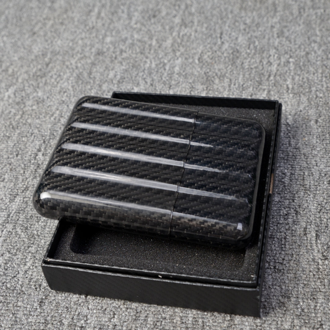 Close-up of a carbon fiber cigar case (capable of holding 5 cigars) featuring a textured pattern, placed in an open black box on a gray fabric surface.