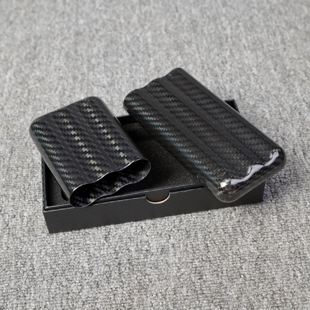 Close-up of carbon fiber cigar tubes with a capacity for 3 cigars, featuring a distinct weave pattern, placed in a black box on a gray fabric surface.