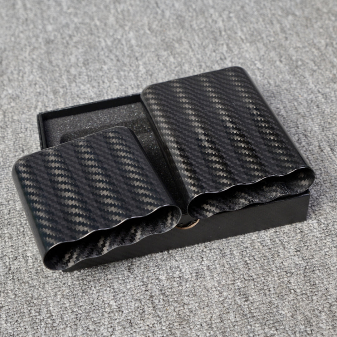 Close-up of carbon fiber cigar tubes with a capacity for 4 cigars, featuring a distinct woven pattern, placed in a black box on a gray fabric surface.