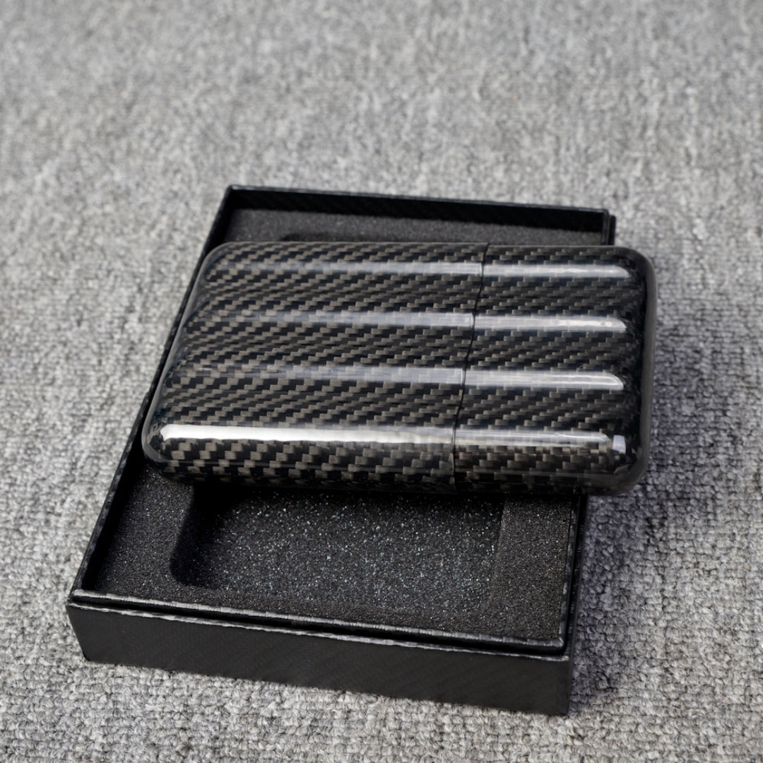 Close-up of a carbon fiber cigar case with a capacity for 4 cigars, featuring a distinct woven pattern, placed in an open black box with foam lining on a gray fabric surface.