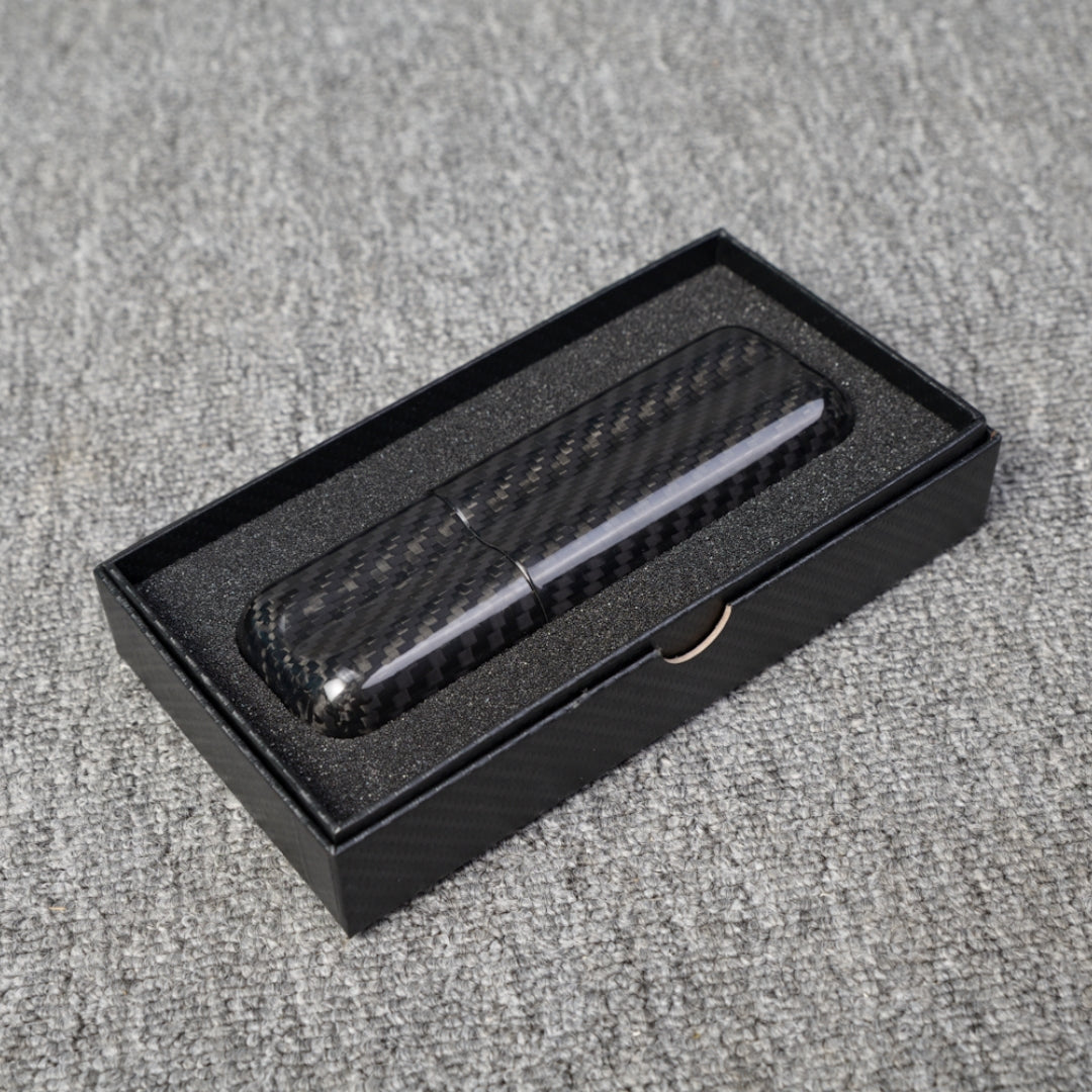 Close-up of a carbon fiber cigar case with a capacity for 2 cigars, featuring a distinct woven pattern, placed in an open black box with foam lining on a gray fabric surface.