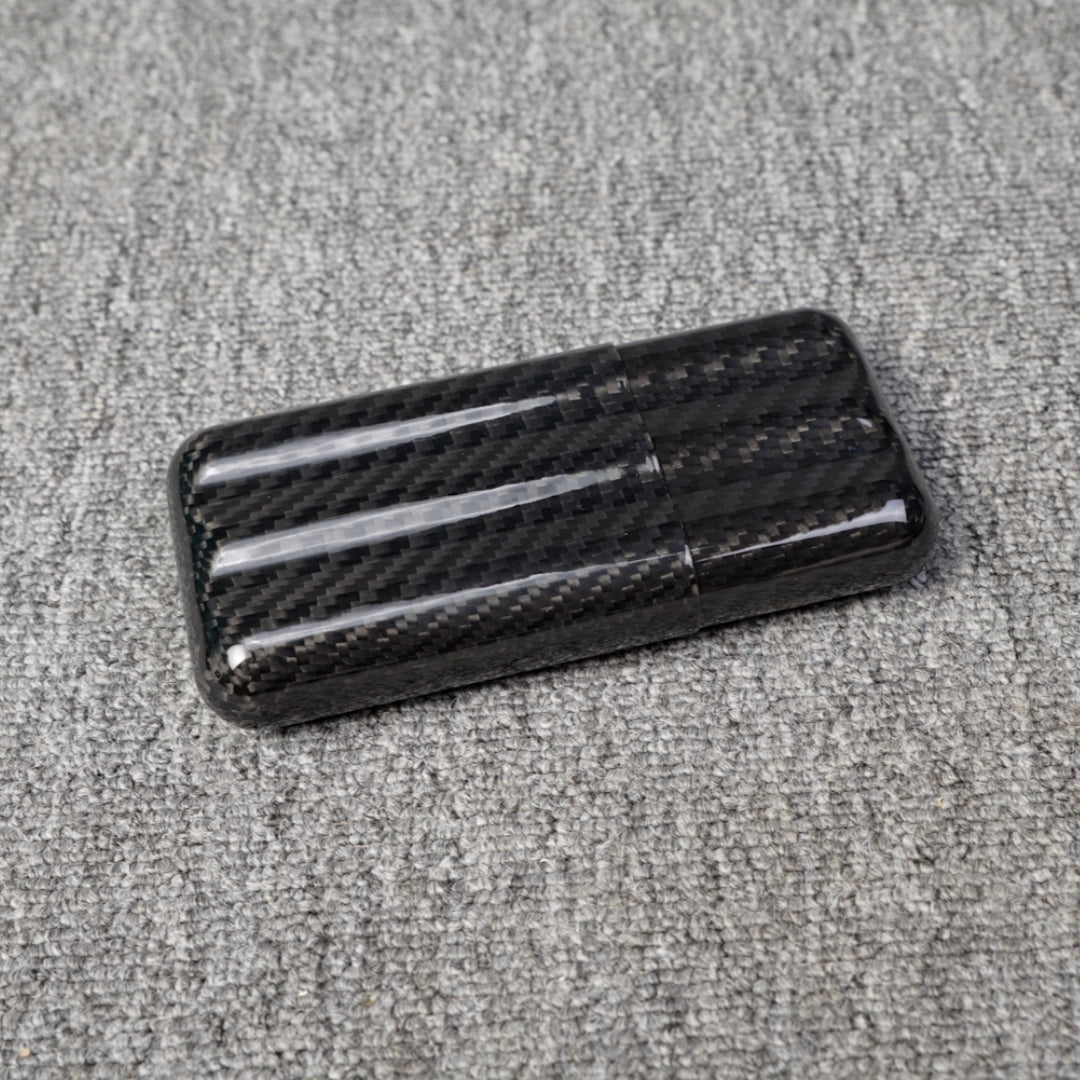 Close-up of a carbon fiber cigar tube with a capacity for 3 cigars, featuring a distinct woven pattern, placed on a gray fabric surface.