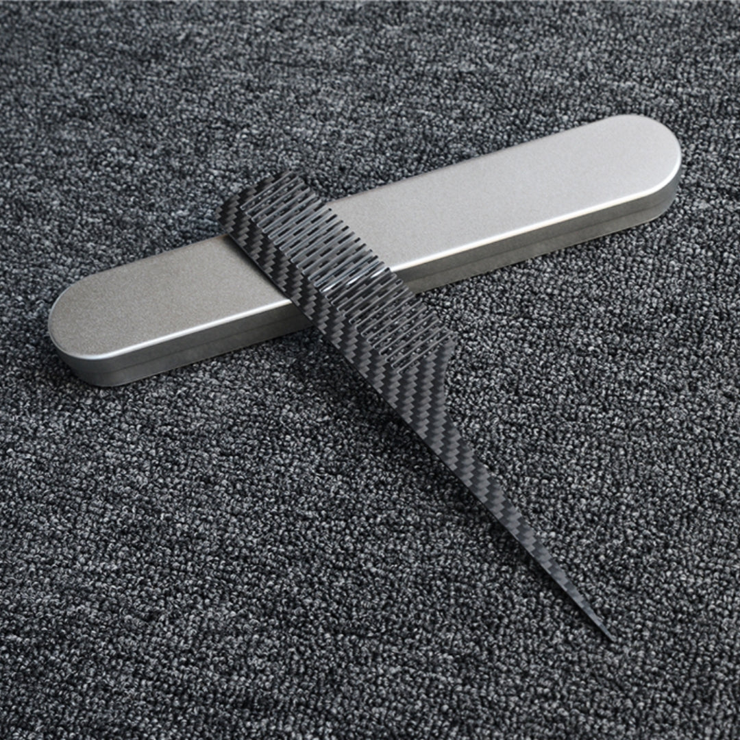Close-up of a carbon fiber comb with a distinct woven pattern, placed next to a silver metal case on a dark gray textured fabric surface.