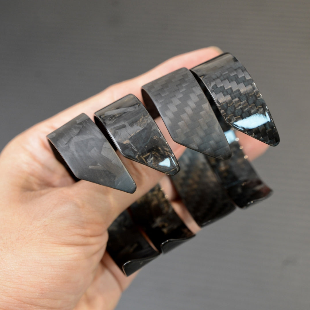A hand holding four black carbon fiber bracelets with distinct weave patterns, displayed against a dark background.