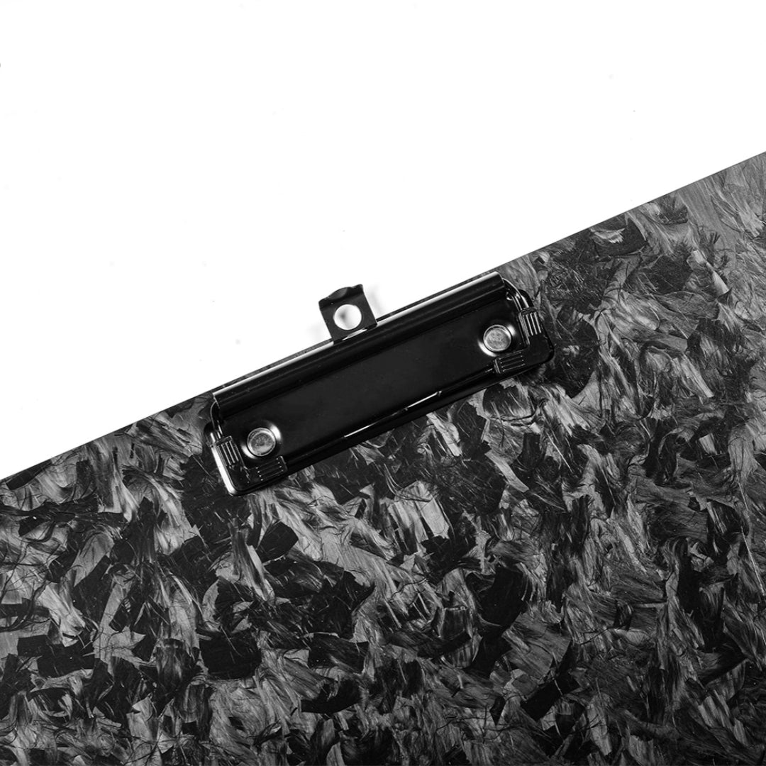 Close-up detail of a forged carbon fiber clipboard with a distinctive marbled pattern and a black metal clip, set against a clean background.