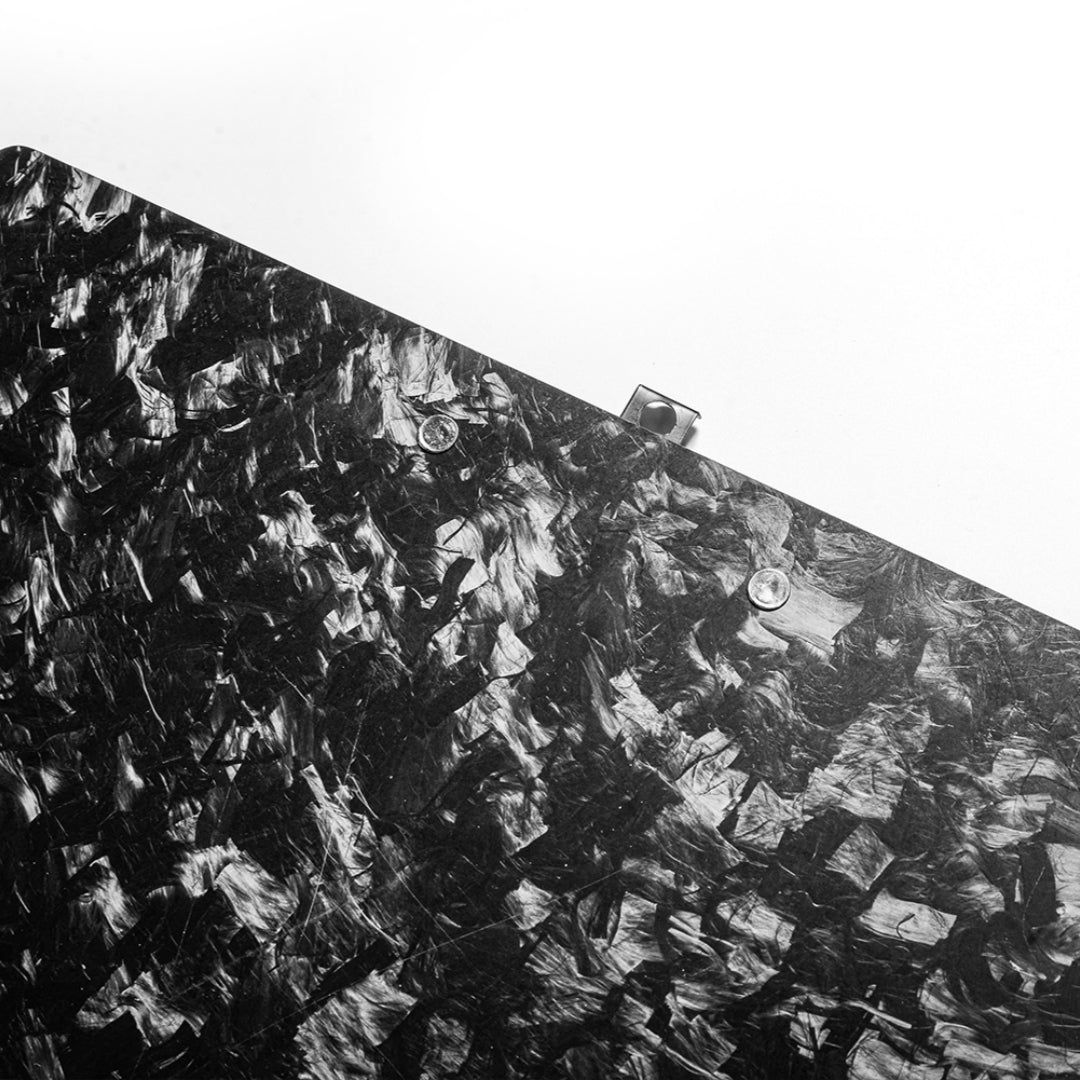Close-up detail of a forged carbon fiber clipboard featuring its distinct chopped texture and metal fasteners, set against a clean white background.