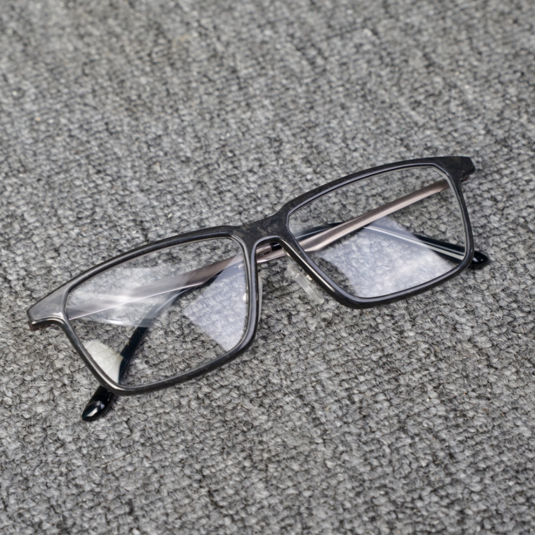 Close-up of a forged carbon fiber eyeglass frame with a sleek black design and clear lenses, placed on a textured gray surface.