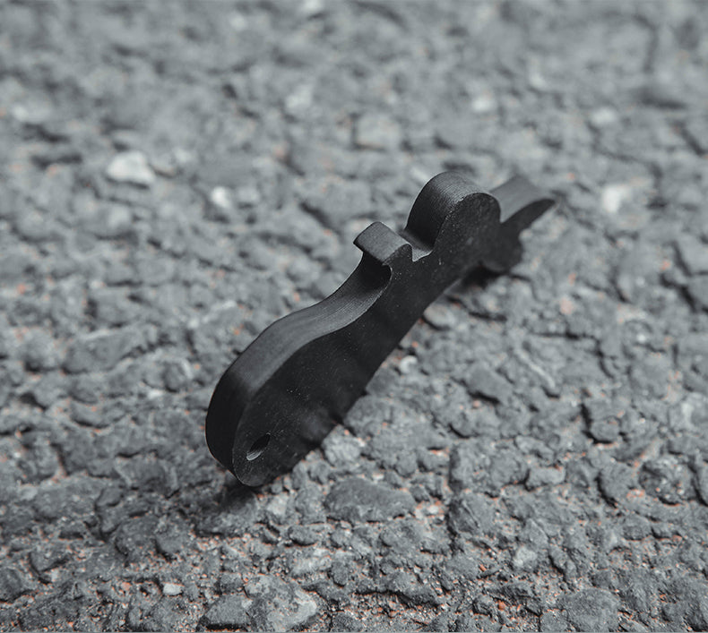 Close-up of a rabbit-shaped 3K carbon fiber keychain with a sleek black finish, placed on a rough asphalt surface.