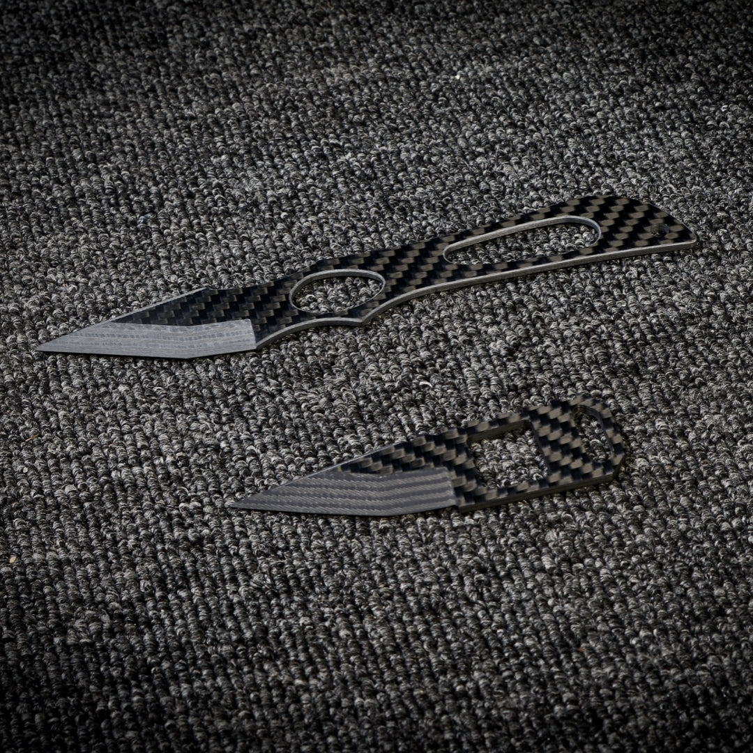 Close-up of two carbon fiber knives with distinctive patterned handles and blades, displayed on a dark textured fabric surface.