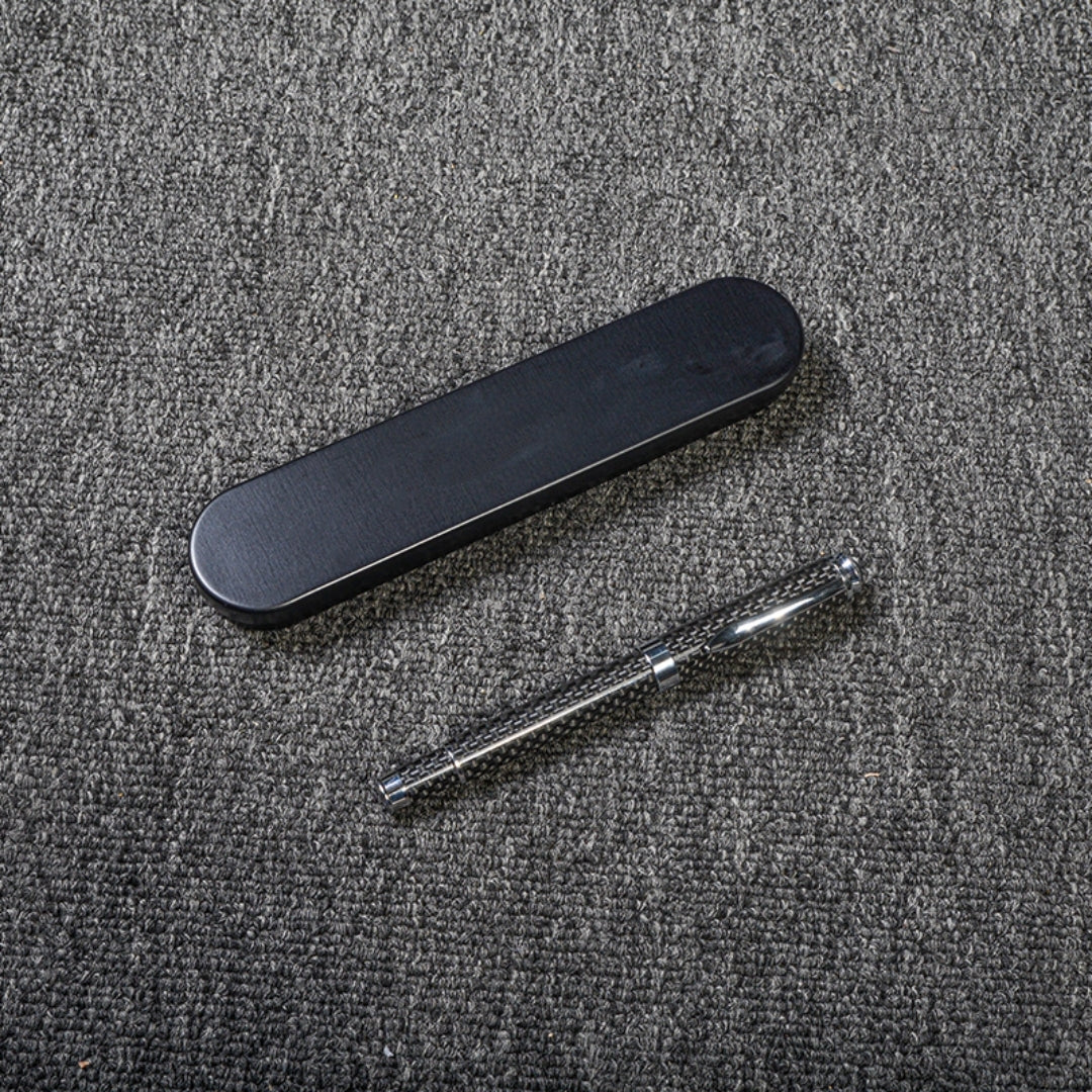 Close-up of a carbon fiber ballpoint pen with a distinct woven texture, accompanied by a sleek black metal case, displayed on a gray textured fabric surface.