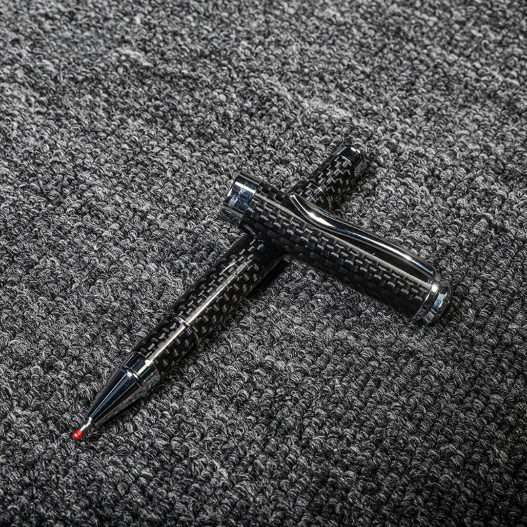 Close-up of a carbon fiber ballpoint pen with a distinct woven texture and metallic accents, displayed with its cap on a gray textured fabric surface.
