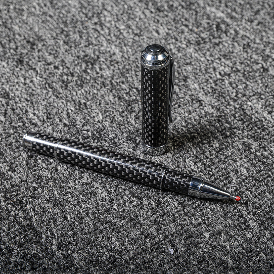 Close-up of a carbon fiber ballpoint pen with a distinct woven texture and metallic accents, displayed with its cap on a gray textured fabric surface.