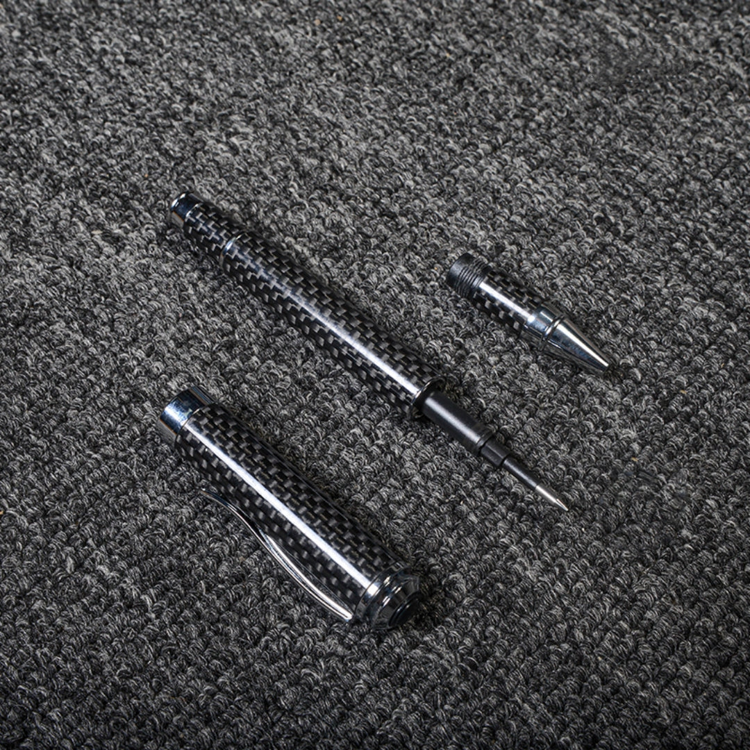 Close-up of a disassembled carbon fiber ballpoint pen with a distinct woven texture and metallic accents, displayed on a gray textured fabric surface.