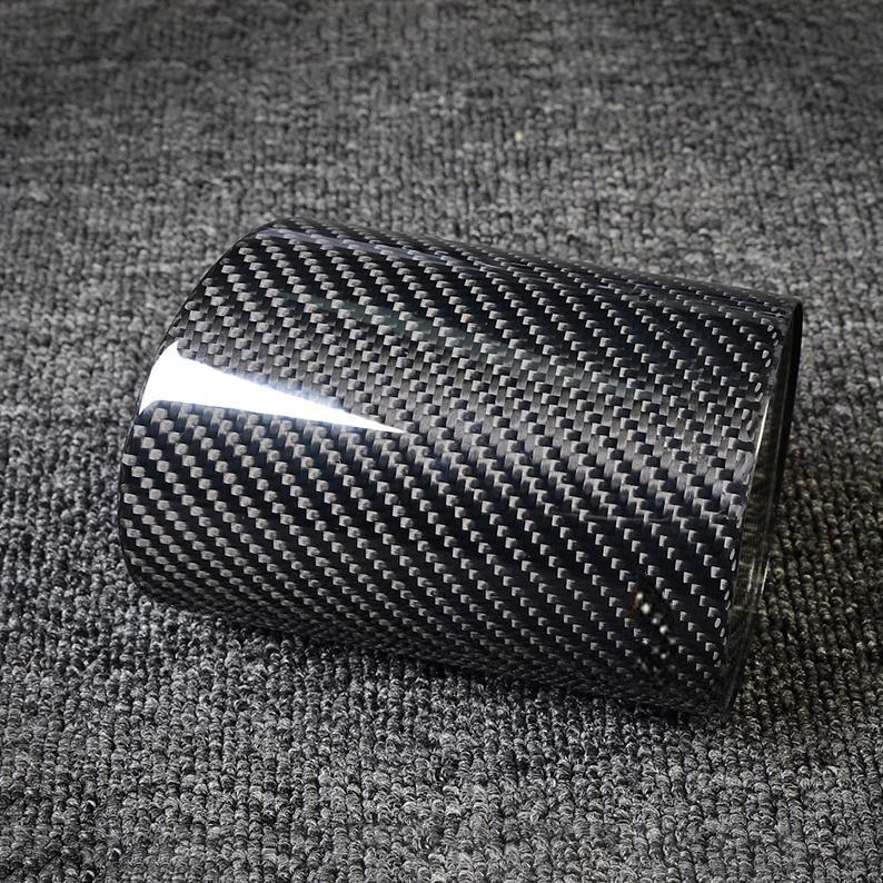 Close-up of a carbon fiber pen holder with a distinct woven pattern, laid on a gray textured fabric surface.