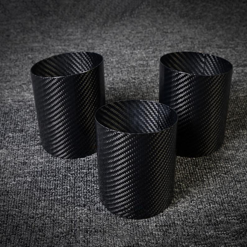 Three carbon fiber pen holders with a distinct woven pattern, displayed on a gray textured surface.