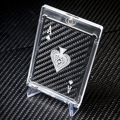 Close-up of a carbon fiber Ace of Spades playing card with silver detailing, encased in a clear protective case and displayed on a carbon fiber textured surface.