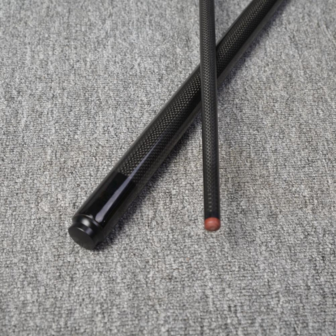 Close-up detail of a two-piece carbon fiber pool cue with a textured carbon fiber pattern, one section featuring a reddish tip, crossed on a gray textured surface.