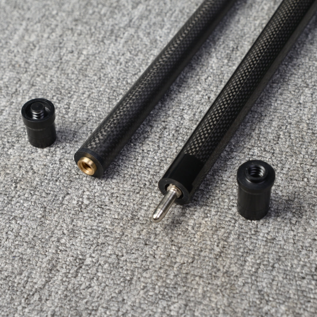 Close-up detail of a two-piece carbon fiber pool cue with a textured carbon fiber pattern, displaying the connecting components, placed on a gray textured surface.