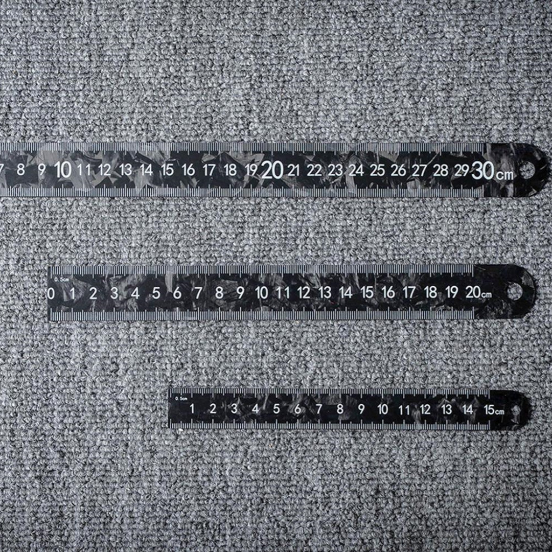 Three forged carbon fiber rulers with distinct lengths and clear measurement markings, placed on a textured surface.