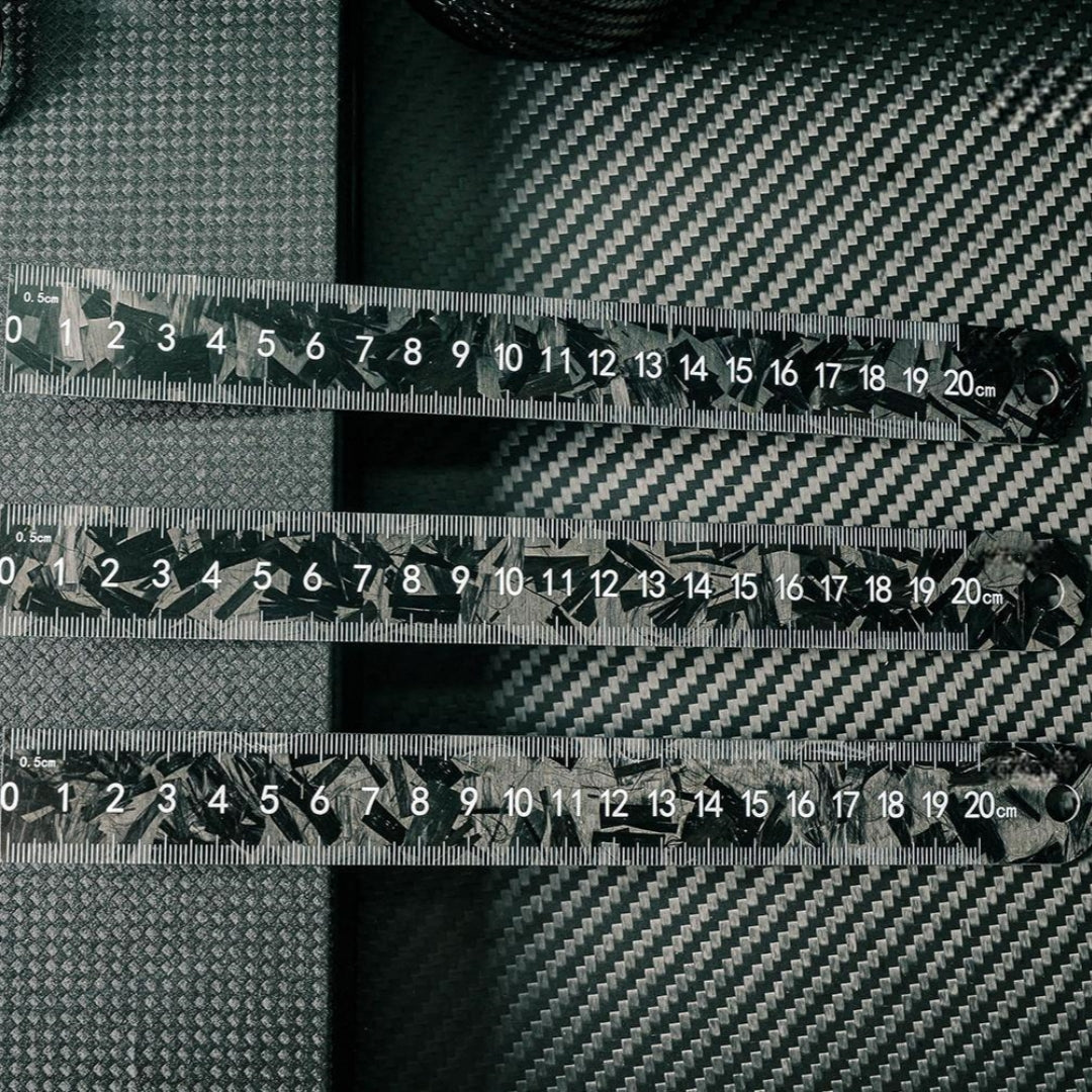 Three forged carbon fiber rulers with distinct patterns and clear measurement markings up to 20 cm, placed on a carbon fiber textured surface.