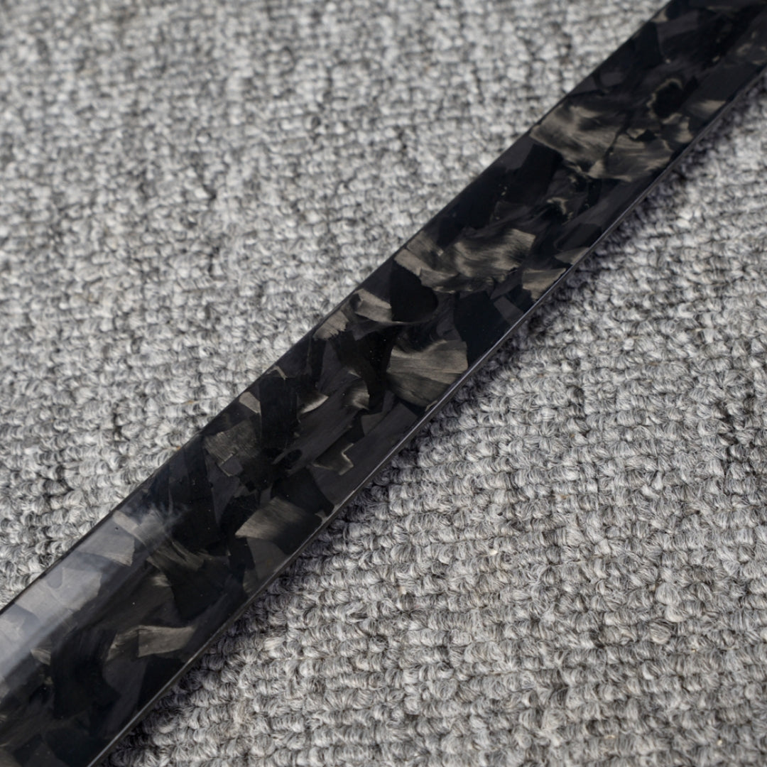 Close-up detail of a long forged carbon fiber shoe horn with a distinct chopped texture, placed on a gray textured fabric surface.