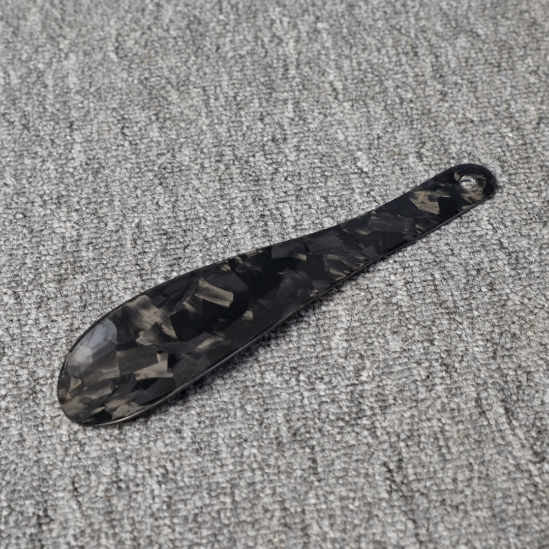 Close-up detail of a short forged carbon fiber shoe horn with a distinct chopped texture, placed on a gray textured surface.