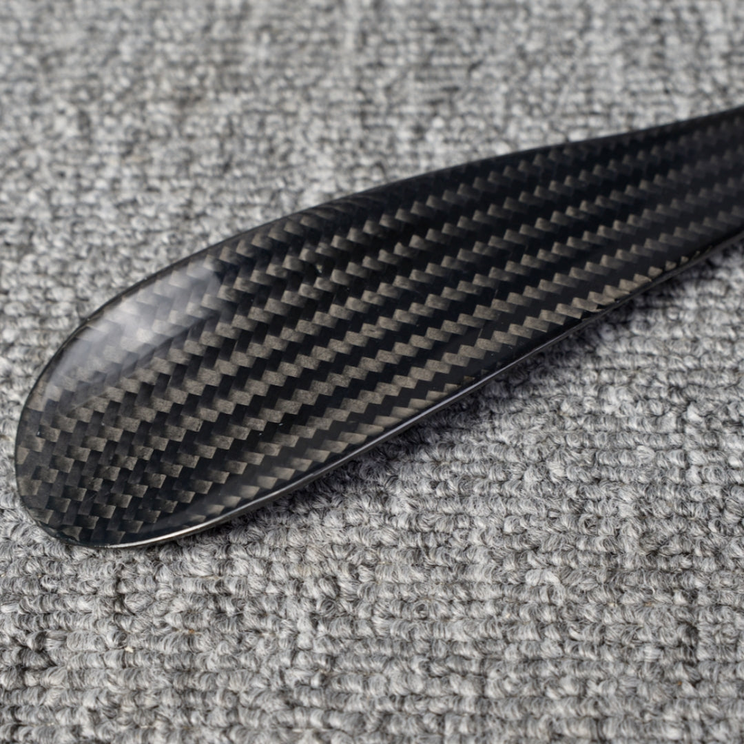 Close-up detail of a short 3K carbon fiber shoe horn with a distinct woven pattern, placed on a gray textured surface.