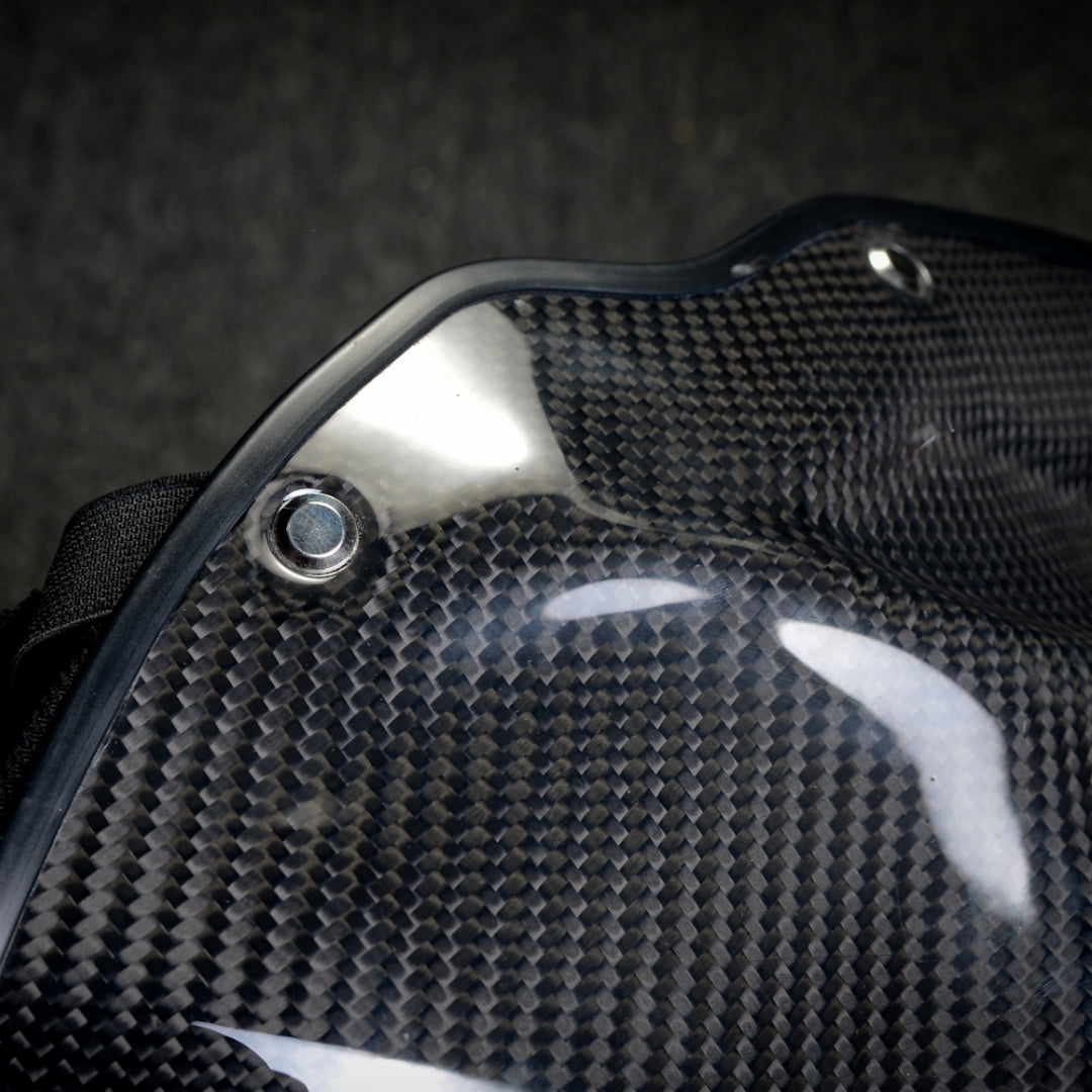 Close-up side detail of a black 3K twill carbon fiber tactical mask, showcasing the woven pattern, glossy finish, and metal rivet.