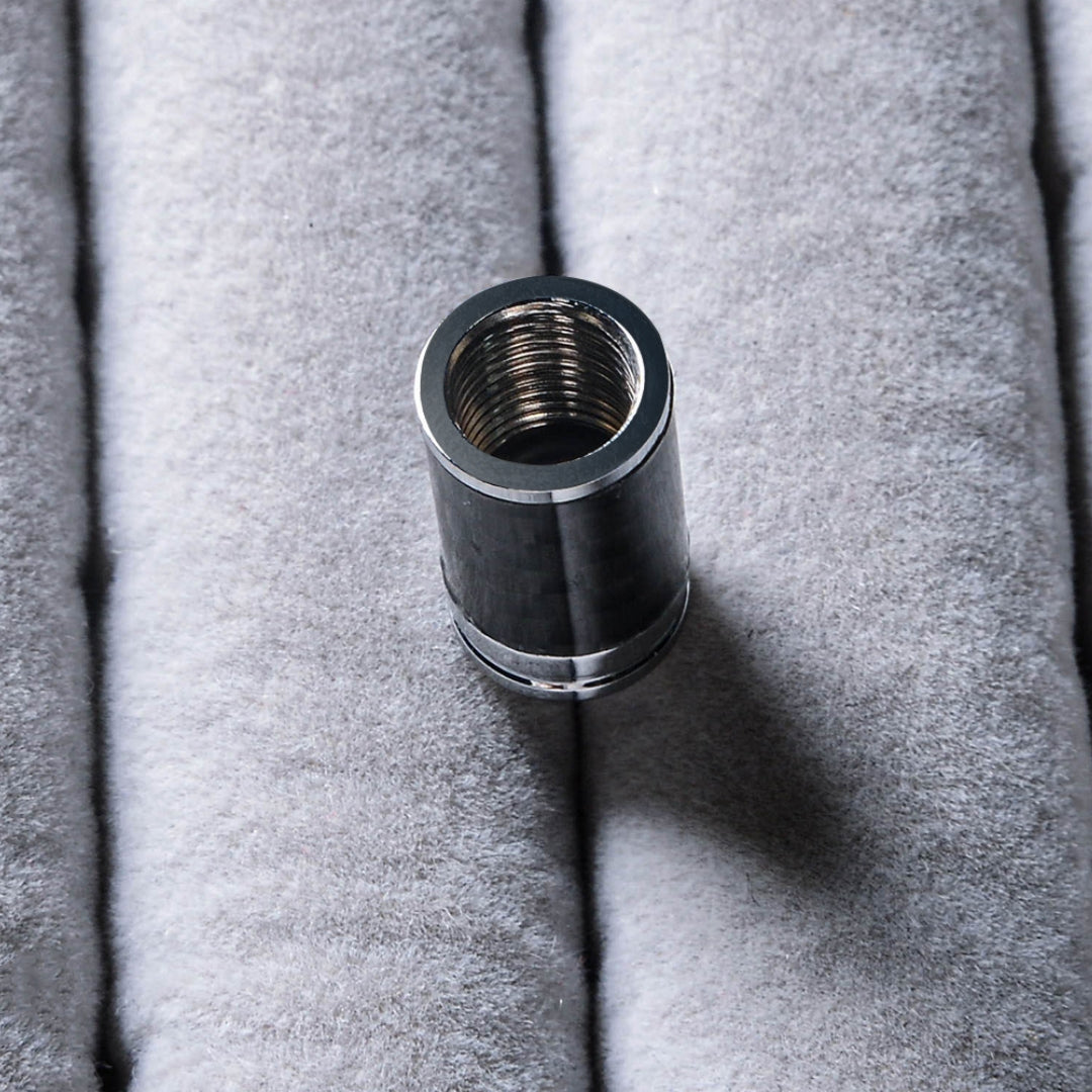 Close-up of a single carbon fiber car tire valve stem cap with metallic detailing, highlighting the threaded interior, resting on a soft gray textured surface.
