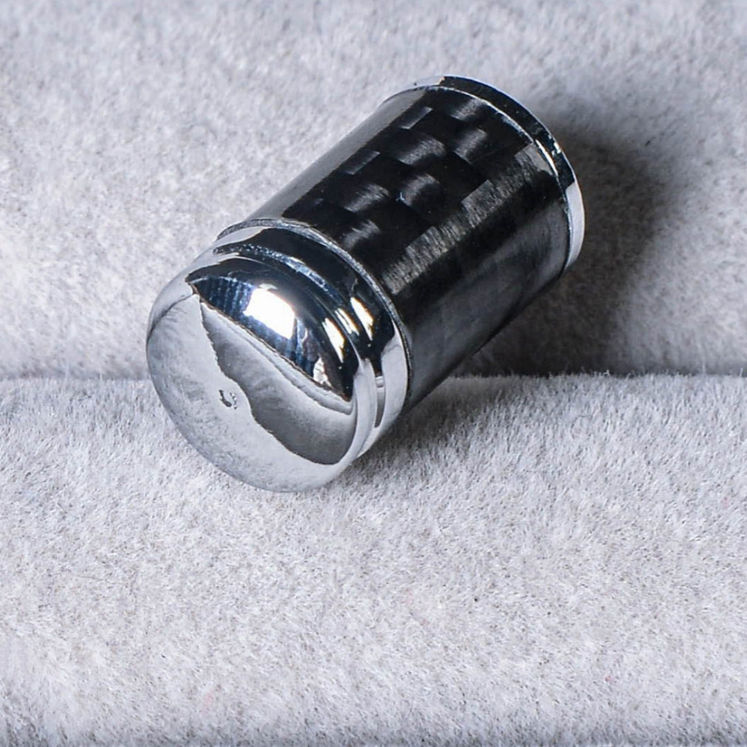 Close-up of a carbon fiber car tire valve stem cap with a shiny chrome-plated top, showcasing the carbon fiber pattern, resting on a soft gray textured surface.