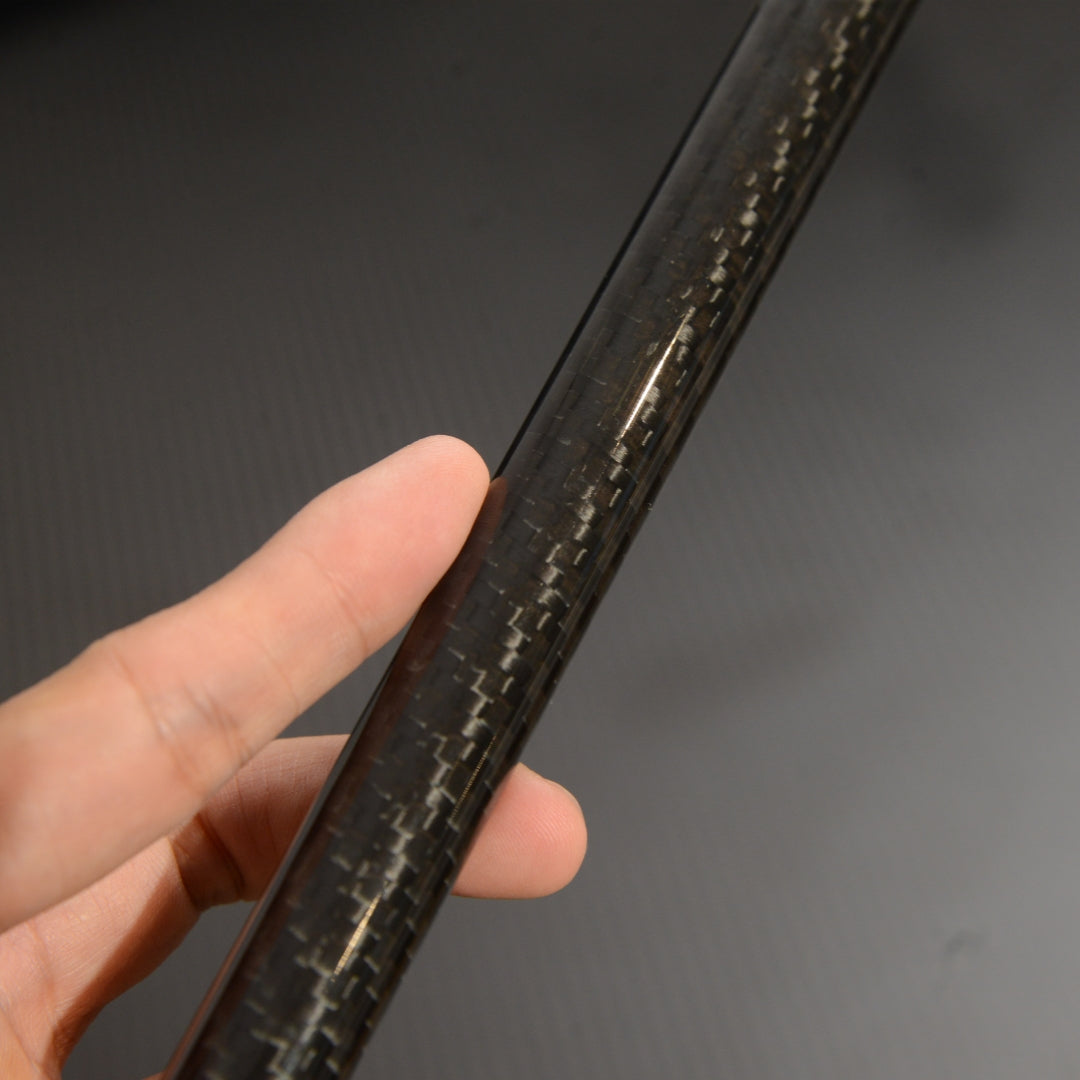 Close-up of a hand holding the shaft of a carbon fiber cane, showcasing the detailed carbon fiber weave pattern against a dark background.