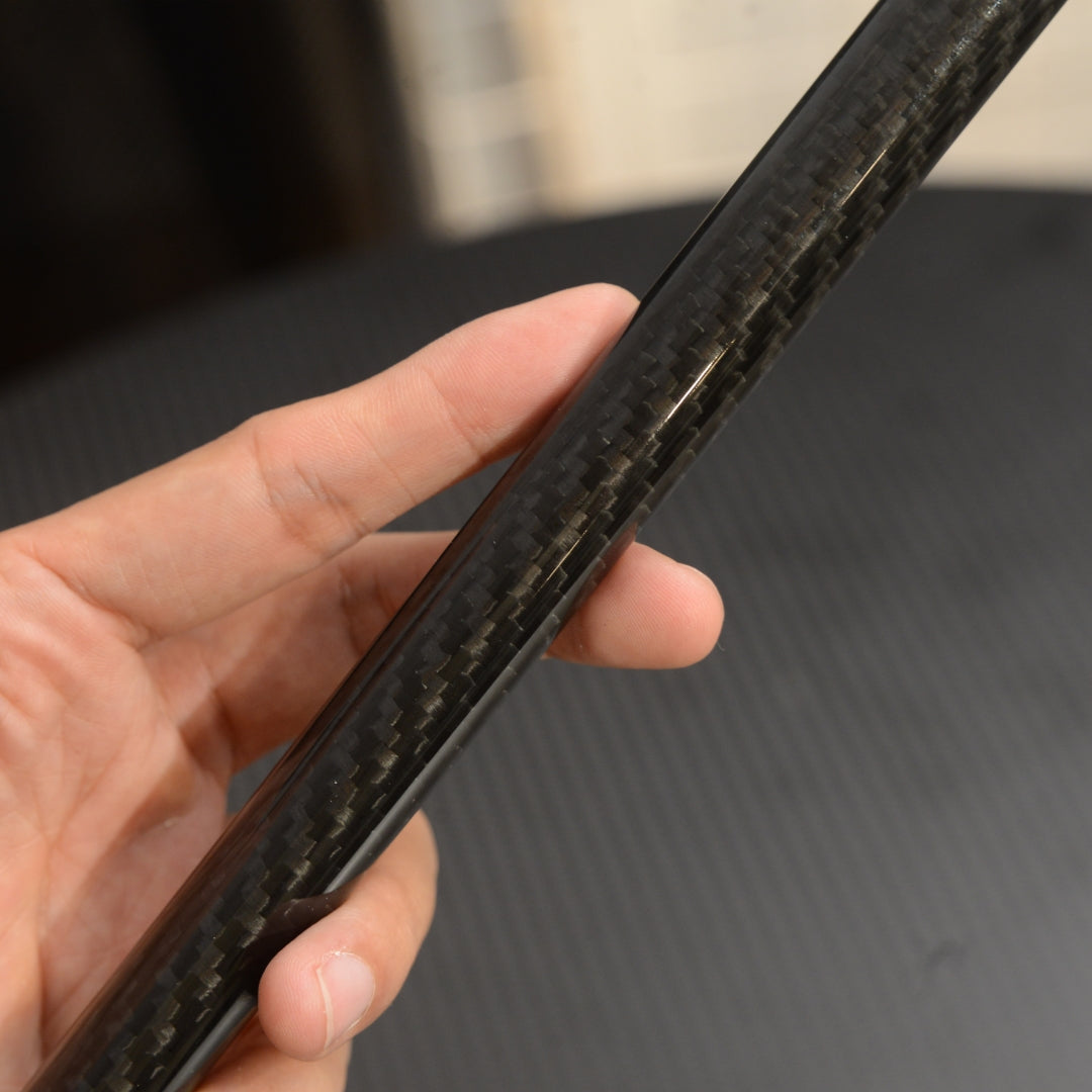 Close-up of a hand holding the shaft of a carbon fiber cane, showcasing the detailed carbon fiber weave pattern against a dark, textured background.