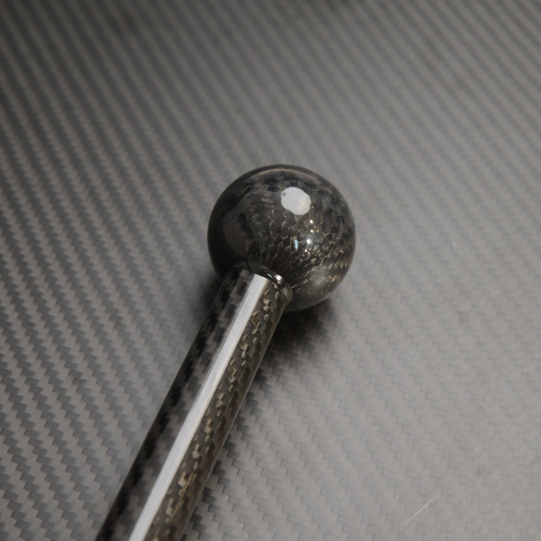Close-up of the spherical top of a carbon fiber cane, showcasing the carbon fiber weave pattern, placed on a carbon fiber textured surface.