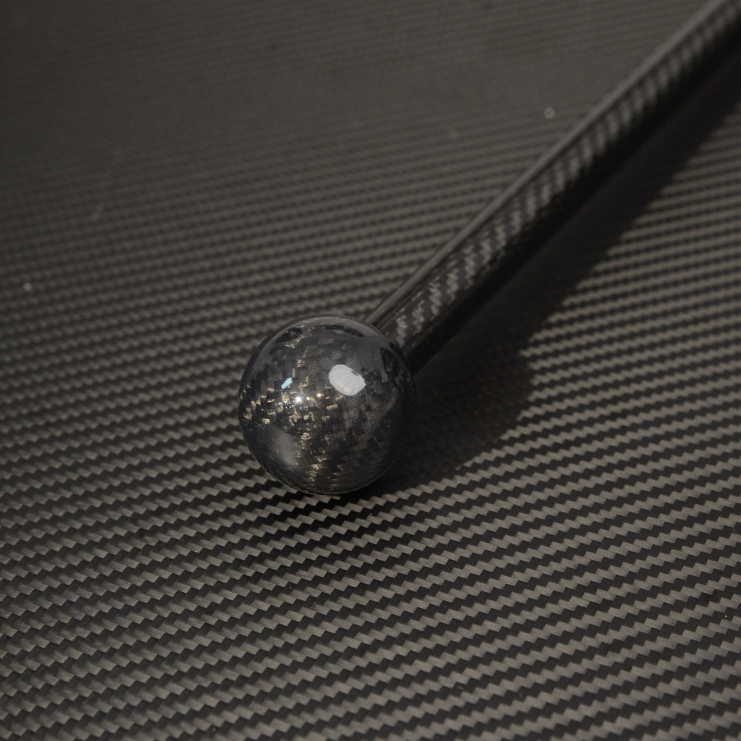 Close-up of the spherical top of a carbon fiber cane, showcasing the carbon fiber weave pattern, placed on a carbon fiber textured surface.