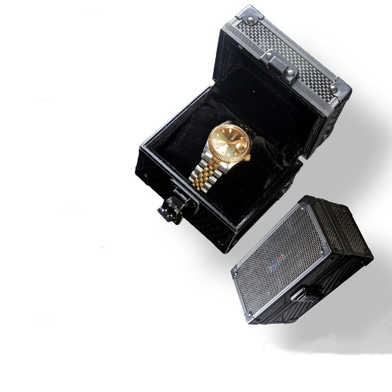 A close-up reveals an open 3K carbon fiber watch box, its lid adorned with a checkered pattern and lined with black velvet, displaying a gold wristwatch within.
