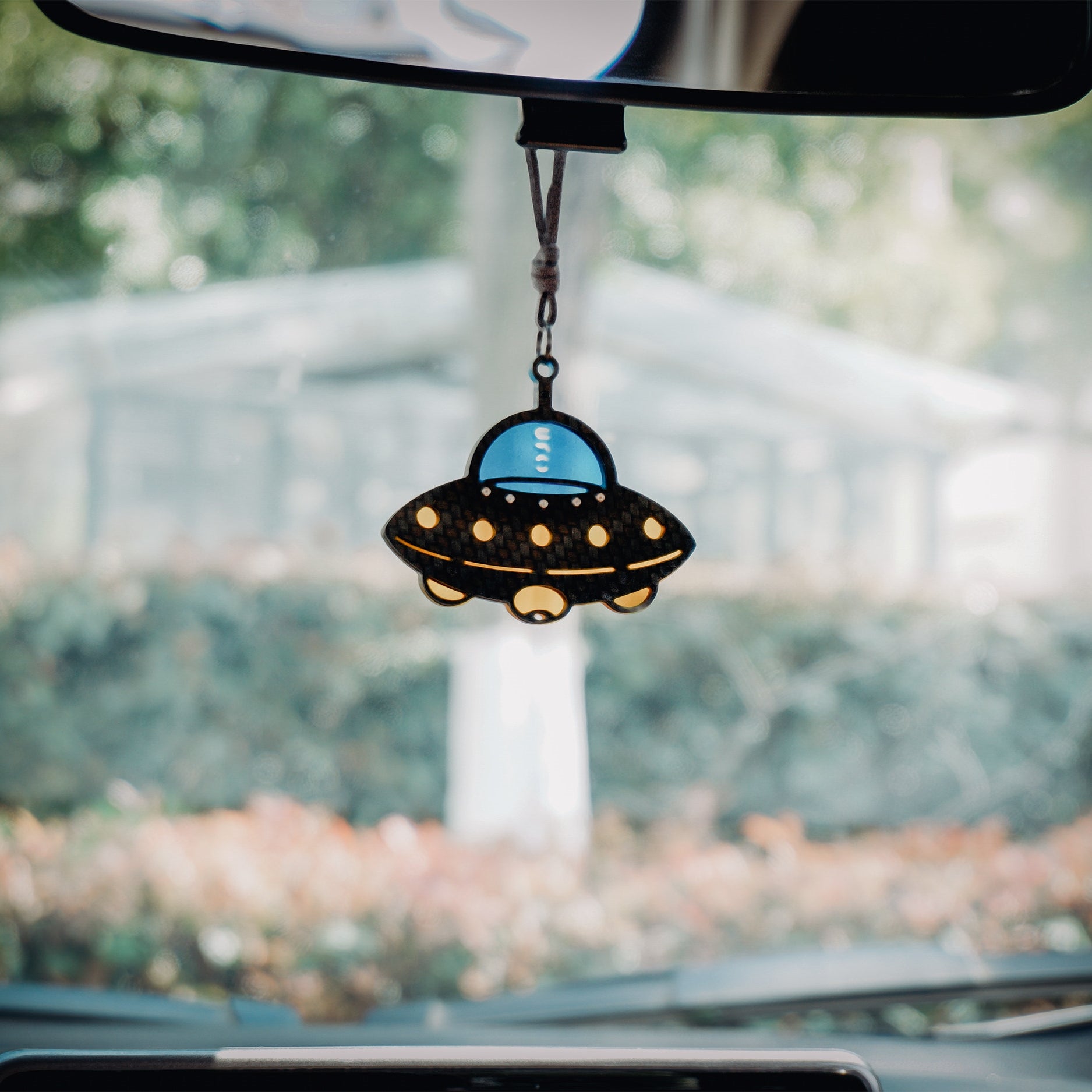 UFO-shaped car rearview mirror hanging accessory: Black carbon fiber-textured saucer body, bright blue cockpit section