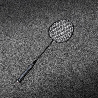 Close-up of a carbon fiber badminton racket with a black frame, shaft, and textured grip, laid on a gray textured surface.
