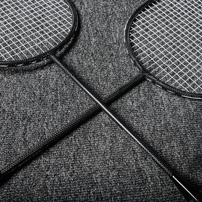 Close-up of two carbon fiber badminton rackets with black frames and textured shafts, crossed on a gray textured surface.